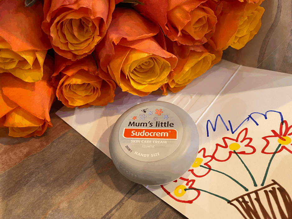  A pot of Mums Little Sudocrem next to some flowers and a child's drawing.