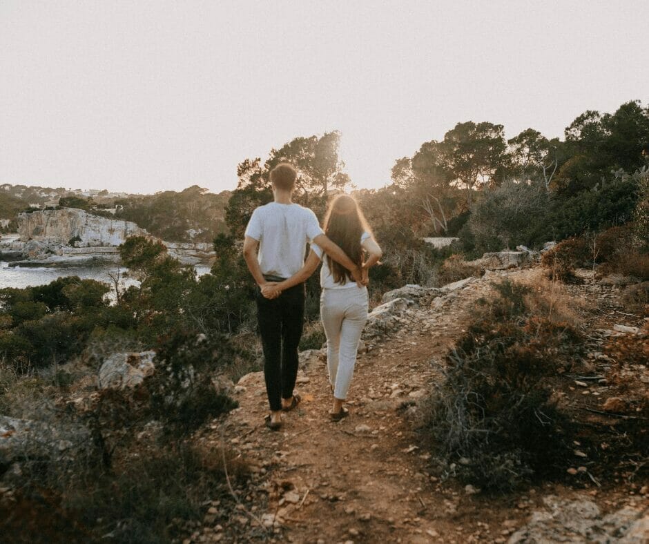 A couple walking together holding hands on a cliff side.