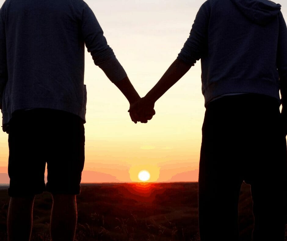 A couple holding hands in front of a sunset.