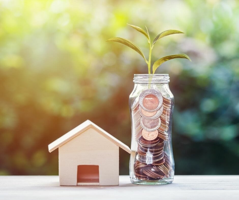A glass of money with a plant shoot next to a model house.
