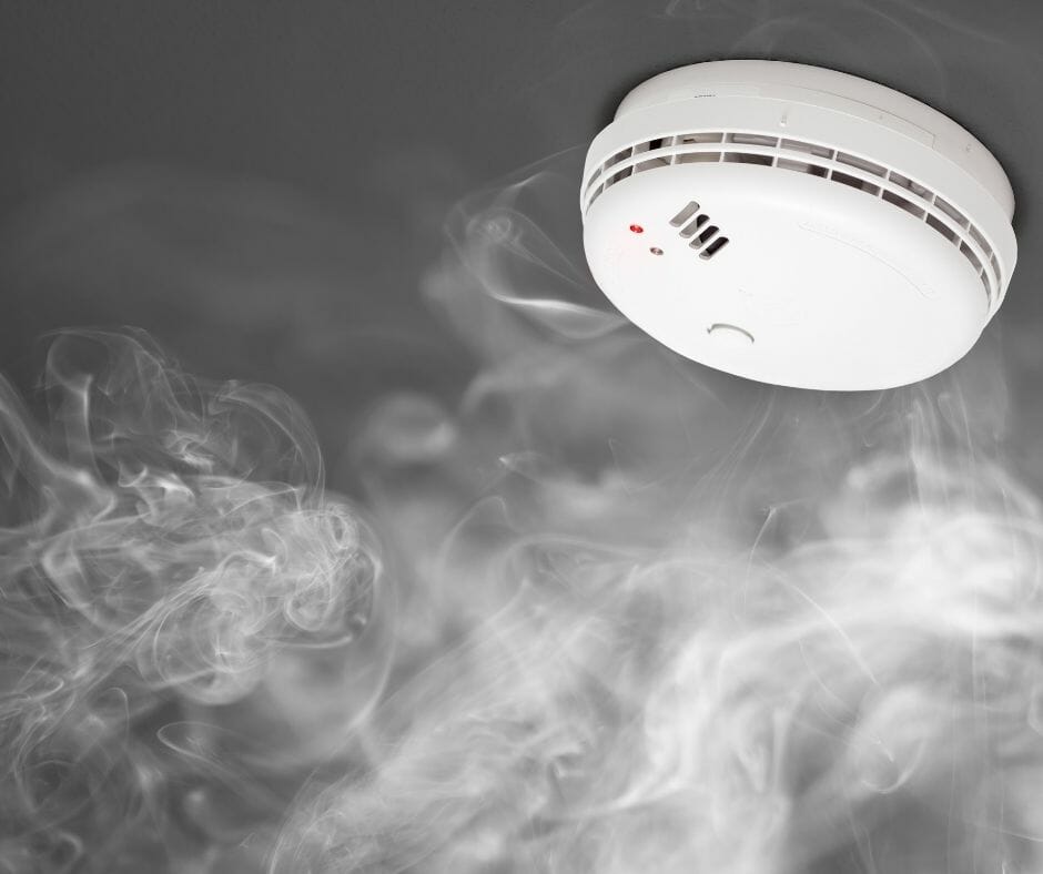 A smoke alarm on a ceiling with smoke next to it.