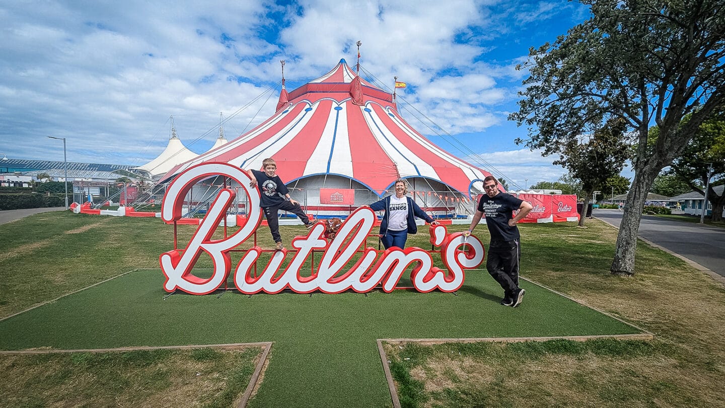 A family of a mum, a dad and their son standing around the Butlins Minehead sign outside the Big Top Circus.